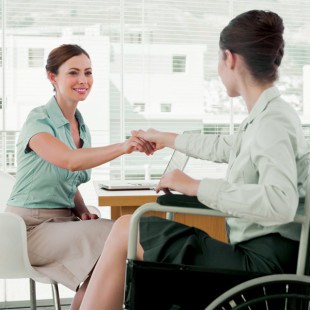 woman professional shaking hands with another woman professional in wheelchair