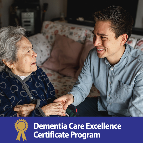 A young man holding hands and smiling at an elderly woman in a cozy living room setting. Text at the bottom reads, "Dementia Care Excellence Certificate Program" with a gold ribbon emblem.