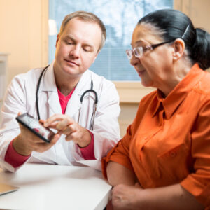 Male doctor showing medical information on a smartphone to an older woman wearing glasses wearing an orange blouse.