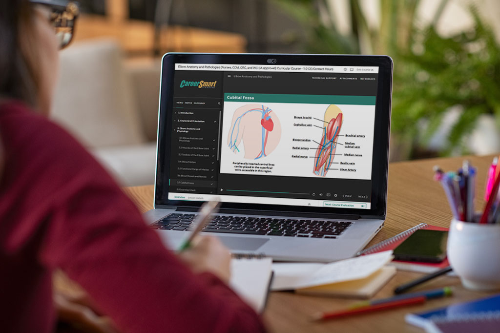 A person is taking notes while viewing an online medical anatomy course on a laptop. The screen shows diagrams and labeled illustrations of the cubital fossa, part of the human elbow, with CareerSmart Learning branding.