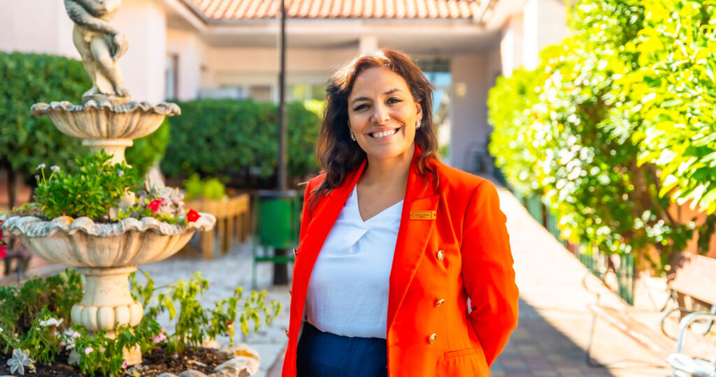RCFE administrator standing in an outdoor courtyard of a residential care community, smiling at the camera.