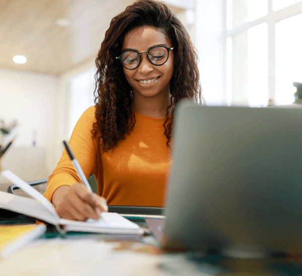 Smiling healthcare professional studying online, taking notes on a laptop for CNA continuing education