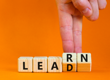 Hand arranging wooden blocks spelling “LEAD RN” on an orange background