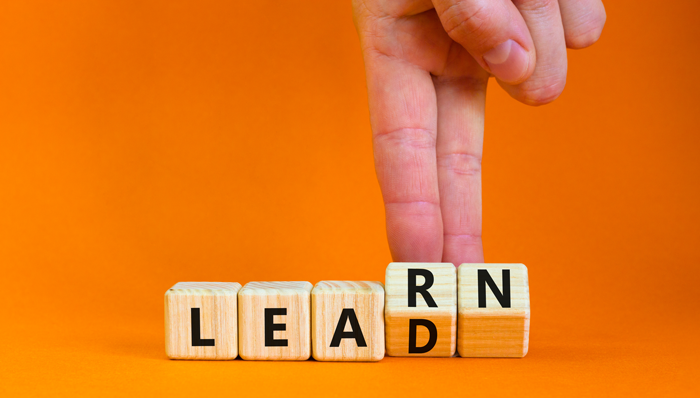 Hand arranging wooden blocks spelling “LEAD RN” on an orange background