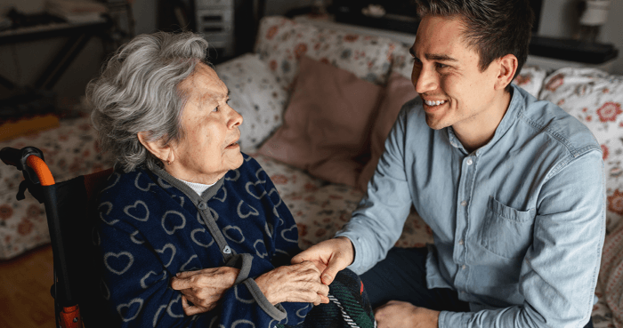Caregiver holding hands with an older adult in a wheelchair during a compassionate dementia care visit.