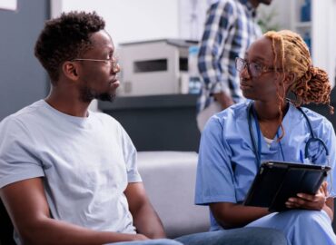 Nurse speaking with a patient while reviewing information on a tablet in an outpatient healthcare setting.