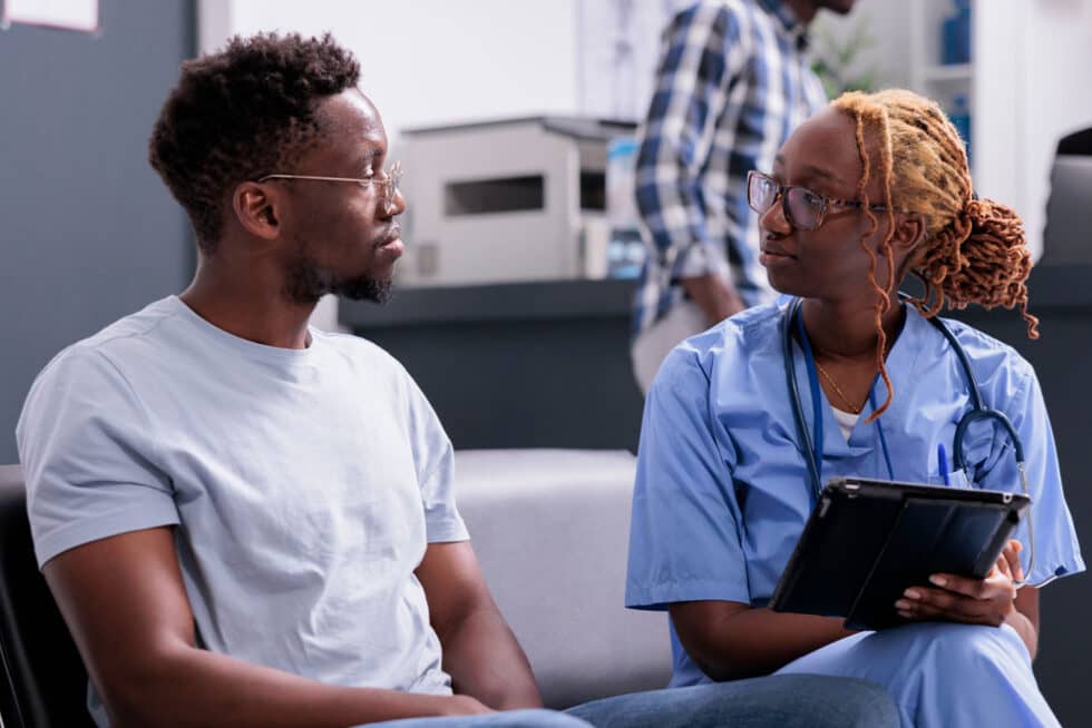 Nurse speaking with a patient while reviewing information on a tablet in an outpatient healthcare setting.
