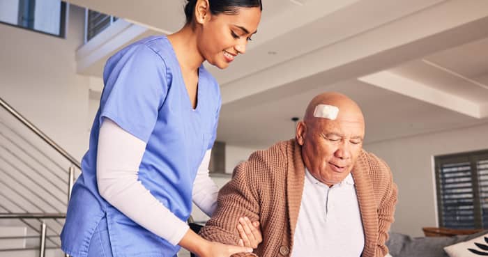 Healthcare professional assisting an older adult with a head bandage, representing California ALW TBI training for assisted living staff
