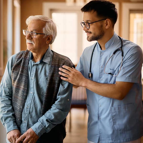 A healthcare professional supports an older adult in a residential care setting. This image accompanies CareerSmart® Learning's California Assisted Living Waiver TBI Training Package, which provides online traumatic brain injury education for staff supporting individuals through California's ALW Residential Habilitation services.