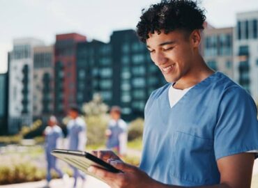 Nurse in blue scrubs using a tablet outdoors while completing online nurse CE.