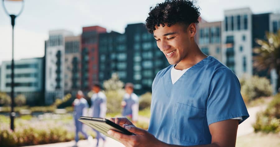 Nurse in blue scrubs using a tablet outdoors while completing online nurse CE.