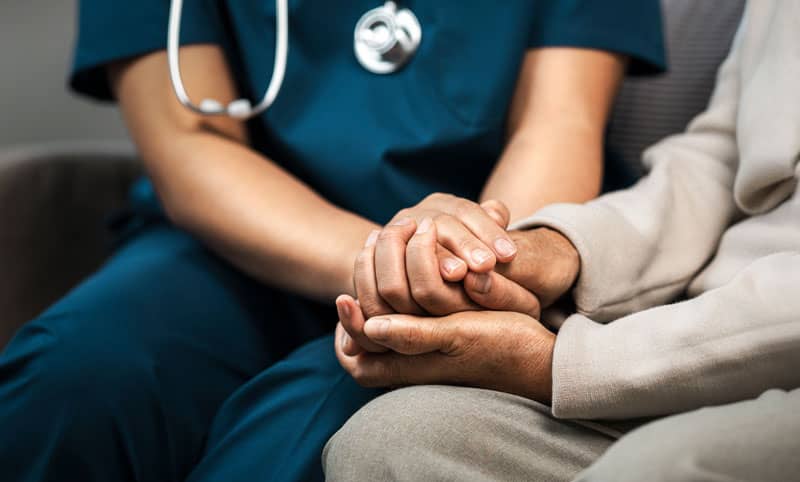Healthcare professional holding a patient’s hands during a supportive conversation about mental health and suicide prevention.
