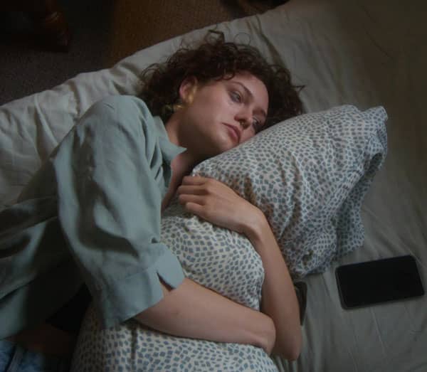 Young adult lying awake in bed holding a pillow, appearing worried and emotionally distressed.