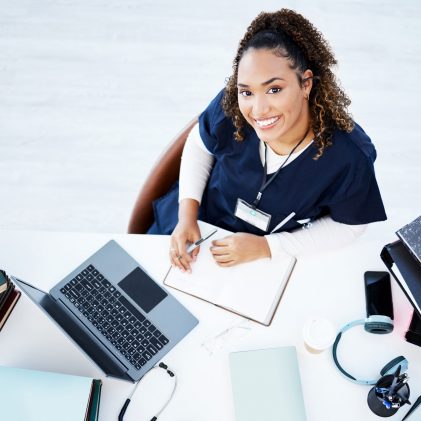 Home health professional reviewing patient documentation at a desk with laptop and medical records.
