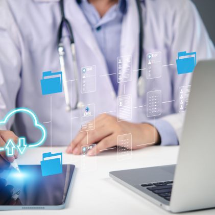 Healthcare professional using a tablet and laptop to access electronic health records and cloud-based data systems