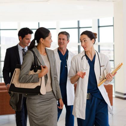 Managed care professionals and healthcare providers walking together in a modern healthcare facility while discussing care coordination and patient support services.