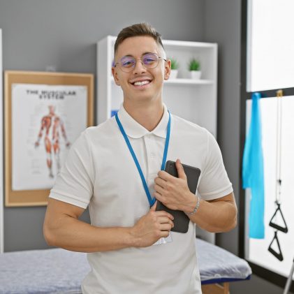 Smiling young hispanic man with glasses, standing confidently in a medical clinic.