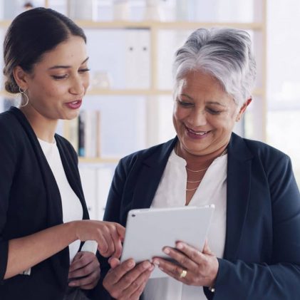 Two healthcare and administrative professionals reviewing workforce training information on a tablet in a collaborative office setting.